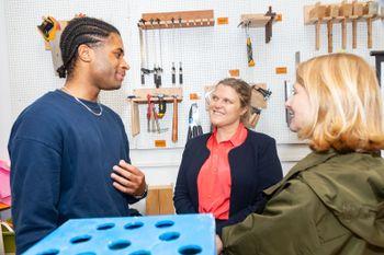 Image of Cllr Grace Williams with two people smiling at Blackhorse Workshop, with tools hanging up in the background